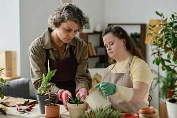 Girl with down syndrome watering green plants together with florist in the room