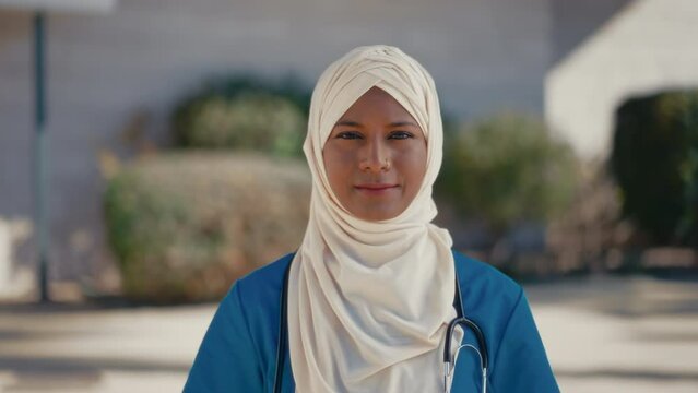 A young Muslim woman, a doctor in a hijab in uniform with a stethoscope, is standing on the street outside the hospital. Medicine and health care.