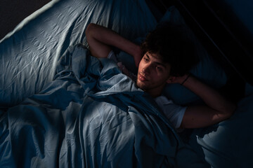 Stressed young man trying to sleep in his bed at night, top view. Insomnia concept