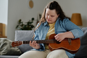 Girl with down syndrome playing guitar sitting on sofa in the living room