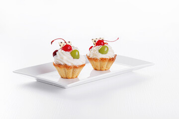 Beautiful cream cakes with cherries and grapes on a plate on a white background