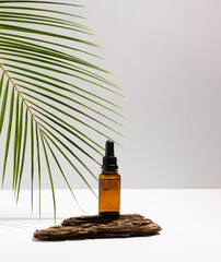 Cosmetic serum Vitamin C in brown glass bottle with pipette dropper on wooden podium. Tropical palm leaf. Beauty concept. Natural skin care cosmetics. Suitable for Product Display.