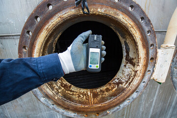 Worker hand holding gas detector inspection safety gas testing at front manhole stainless tank - obrazy, fototapety, plakaty