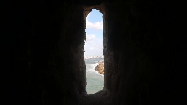 A View Through a Narrow Opening in a Stone Wall to the Sea and a Distant City