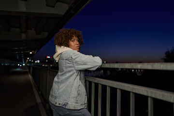 Black woman standing on the bridge at night and looking at camera