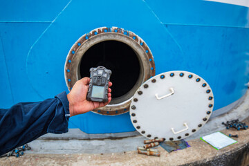 Worker hand holding gas detector inspection safety gas testing at front manhole tank