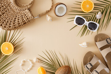 Warm-weather retreat concept. Top view flat lay of beach essentials, juicy oranges, coconuts, seashells and tropical leaves on pastel beige background with empty space for message