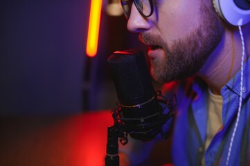 A video blogger records content in his studio. The host of the video blog is a young man who is...