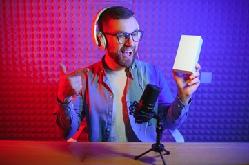 Young male technology blogger recording video blog or vlog about new smartphone and other gadgets at home studio. Blogging, Work from Home concept. Focus on gadgets at the table. Web Banner