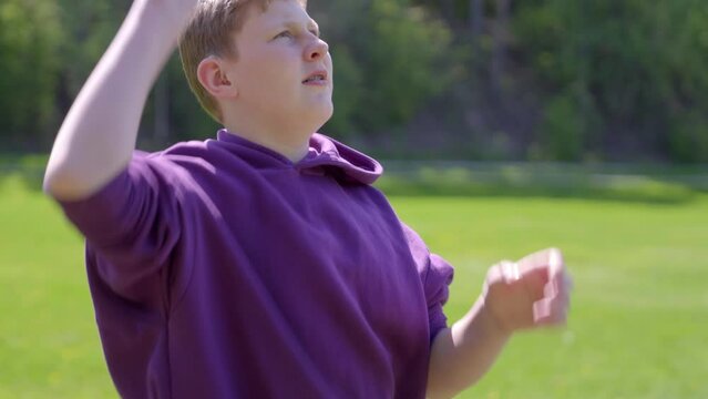 A medium close up of a teenage boy wearing hearing aid throwing a frisbee in a green field.