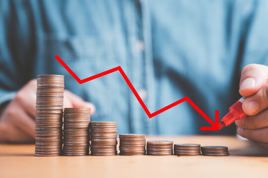 Businessman writing red decreasing arrow on coins stacking for business loss profit investment and economic recession concept.
