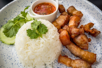 Closeup of Crispy Fried Pork on Rice with Fish Sauce and Coriander Cucumbers and chili paste on the plate on the table