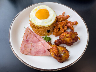 Fried rice with fried eggs, vegetables, hot dogs, ham and fried chicken shoots on a plate on the table.