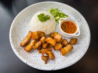 Crispy Fried Pork on Rice with Fish Sauce and Coriander Cucumbers and chili paste on the plate on the table