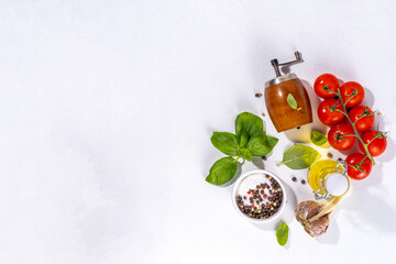 White cooking background with useful cooking italian Mediterranean ingredients - tomatoes, basil leaves, greens, olive oil, salt, pepper, garlic, flat lay white table top view copy space 