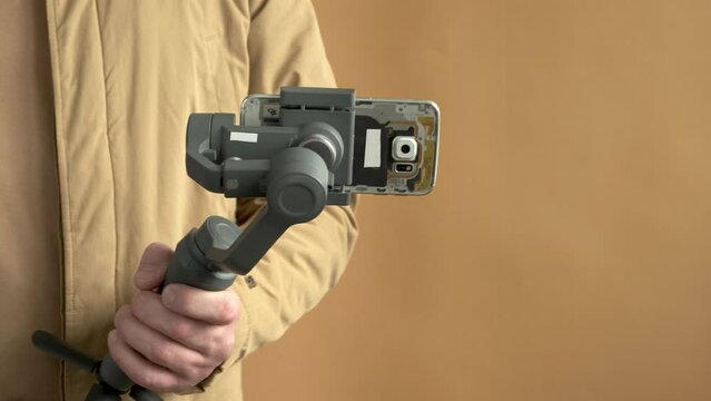 Man filming with a smartphone using a gimbal stabilizer on yellow background. Using three-axis electronic stabilizer to make vlogs or video shooting.