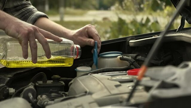 Man pouring some windshield washer fluid in the special compartment under the hood of the car. Filling liquid reservoir tank with antifreeze to spray the car screen