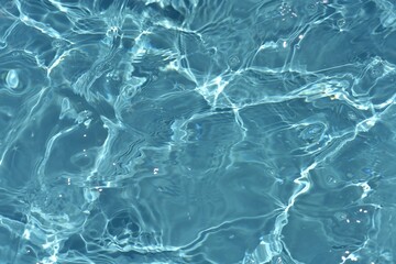 Blue water with ripples on the surface. Defocus blurred transparent blue colored clear calm water surface texture with splashes and bubbles. Water waves with shining pattern texture background.
