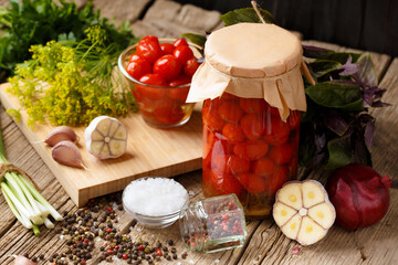 Pickled cherry tomatoes in jars and spices on a wooden background