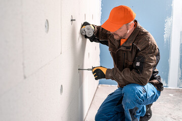 A construction worker inserts a dowel for thermal insulation to prepared hole at the mineral...