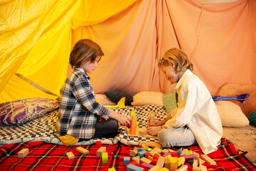 Two young boys are messing around with toy airplanes inside a big blanket tent which has very...