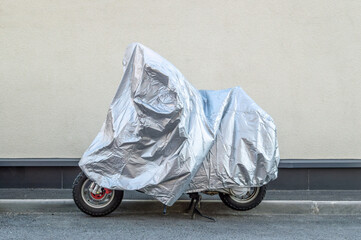 The motorcycle is covered with a silver cover against the wall