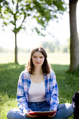 Happy young woman in the park sitting in the grass looking at Camara, concept study outdoors