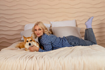Attractive blonde hair girl and a Welsh corgi Pembroke dog are lying on the bed together.