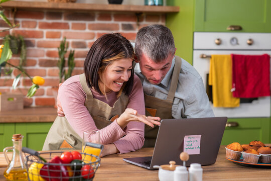 At the kitchen island excited couple smiling large discussing with someone on video chat from the laptop they says hi and kissing on air