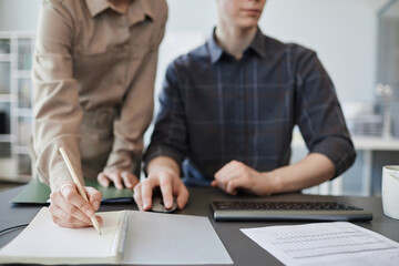 Obraz premium Closeup of young woman taking notes in notebook while reviewing project in office, copy space