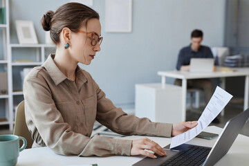 Side view portrait of elegant young woman wearing glasses while reviewing documentation in office, copy space