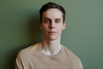 Minimal closeup portrait of young man looking at camera against green, copy space