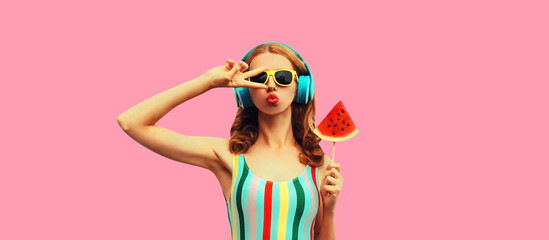 Summer portrait of stylish woman in headphones listening to music blowing her lips with juicy...