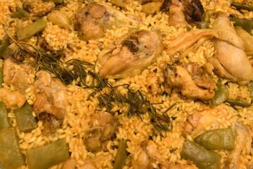 Obraz na płótnie Canvas Close-up of a Valencian paella with rice, chicken meat, vegetables and a rosemary branch