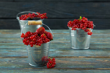 Full three  buckets of ripe red currants, strawberries and blackberries on a blue  wooden aged background