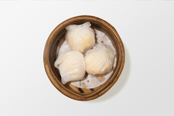 Hakau is a Chinese dumpling made from shrimp wrapped with rice paper roll served on a bamboo bowl on white background. Top view close up detail.
