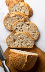 Close-up, top view slices of sourdough bread on a wooden board on a white marble background. Organic baked goods. Wheat grain natural bread.