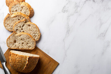 Sourdough Wheat Bread sliced on a wooden cutting board with a knife. Healthy natural bread made from organic products. Copy space banner on marble white background. Top view.