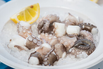 Plate of raw fresh pieces of octopus with lemon and ice ready to eat in a fish market in Bari, Puglia, Italy