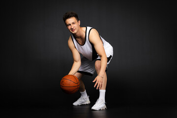 Handsome young basketball player in white sportswear. Isolated on black background.