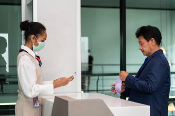 Fototapeta premium Airline stewardess working on the ground wearing face masks checking passports for Asian male passengers outbound-check-in ticketing with boarding pass counters at airport terminals