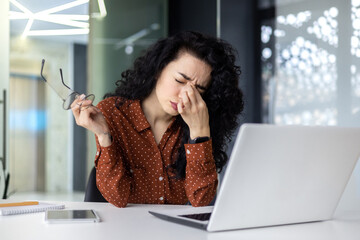 Overtired hispanic woman at work, business woman in glasses holding hands on head, having severe...