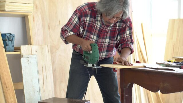 Lifestyle aging society concept, Asia elderly man focus on his hobby at carpentry home studio, people spend free time creating DIY toy for kids after retirement, aged people with silver hair working