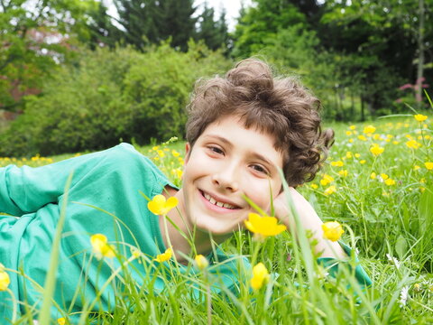 Cheerful little boy lying on the grass, camomile and celandine flowers, smiling. Happyness, childhood