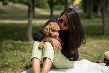 A beautiful Asian girl (Kazakh) holds a dog (mini poodle) in her hands. Summer portrait of a young woman in the park.