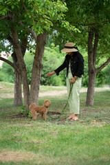 A beautiful Asian girl (Kazakh) walks with her dog (mini poodle). Summer portrait of a young woman in the park.