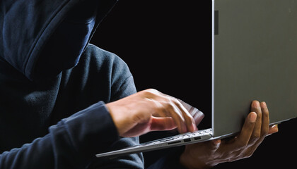 Hacker spy man one person in black hoodie sitting on a table looking computer laptop used login...