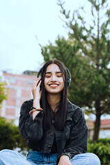 Portrait of a young woman listening to music on wireless headphones on a sunny afternoon in a park in South America.