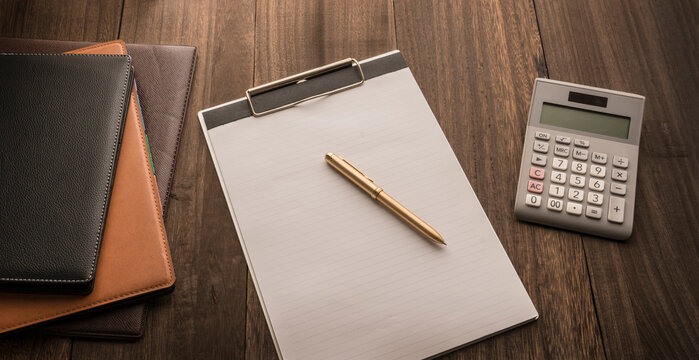 notebooks, notepad on clipboard and calculator on a wooden base.