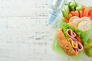 Healthy food for school lunch concept. Healthy bread, meat sandwich with cheese, apple, fresh cucumber, carrots, nuts in container, water and yogurt on kitchen background. Back to school concept.